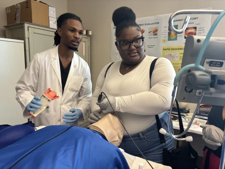 Jerrian Reedy, left, a student at the University of Mississippi School of Medicine, assists Dorothy Gray, a student at Northside High School in the Mississippi Delta, as she practices intubation in a simulation lab. Gray, who is interested in pursuing a career in the mental health care field, attended the University of Mississippi School of Medicine’s annual African American Visit Day in April. Lauren Sausser for KFF Health News